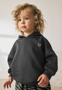 Dark gray hoodie with a smiley face logo on the chest, paired with striped green and black pants, featuring a relaxed fit and soft fabric texture.