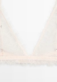 Lace bralette in light pink with a triangular shape; features frayed edges and floral patterns along the trim for added detail.
