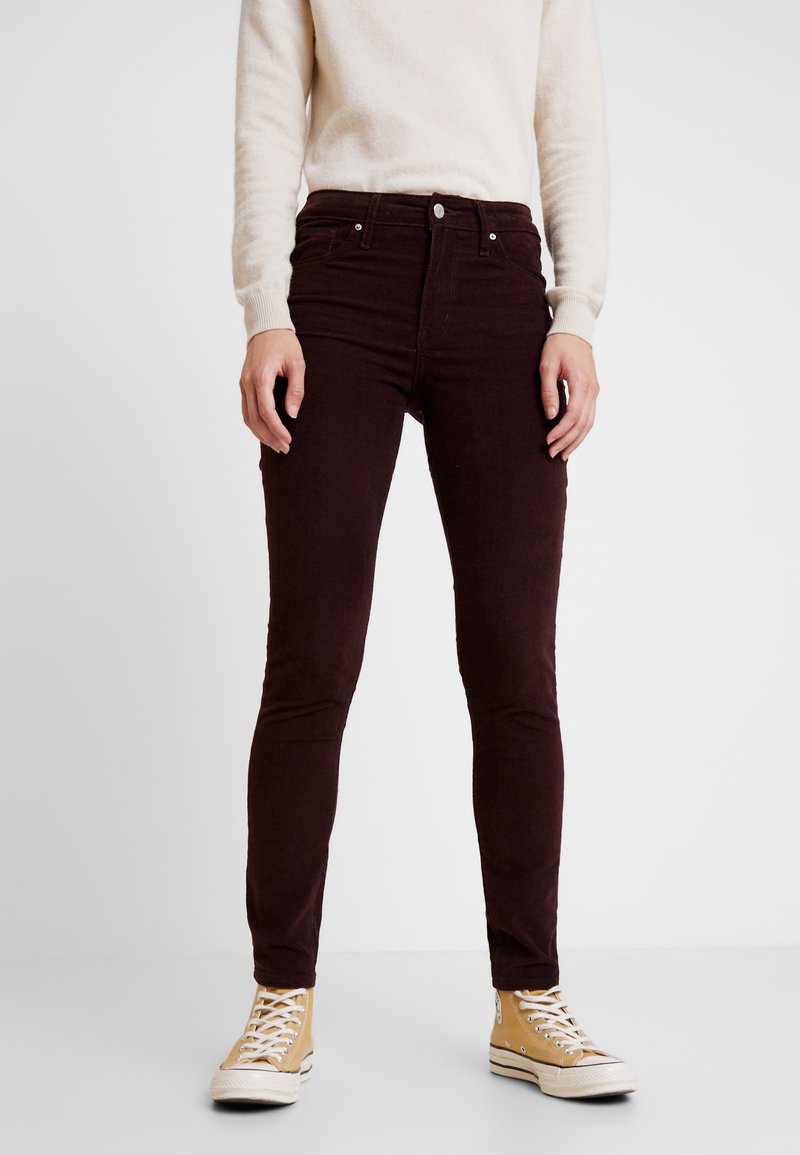 Pantalones de pana burdeos de corte slim con diseño de cinco bolsillos, que cuentan con cierre de botón, combinados con zapatillas de alta beige.