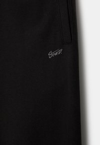Schwarze Jogginghose aus weichem Stoff, mit einem dezenten grauen Logo auf der linken Seite, elastischem Bund und seitlichen Taschen.