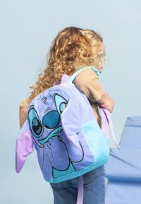 Sac à dos violet et bleu avec un design en peluche de personnage de dessin animé, doté de grandes oreilles, d'un visage proéminent et de bretelles ajustables.