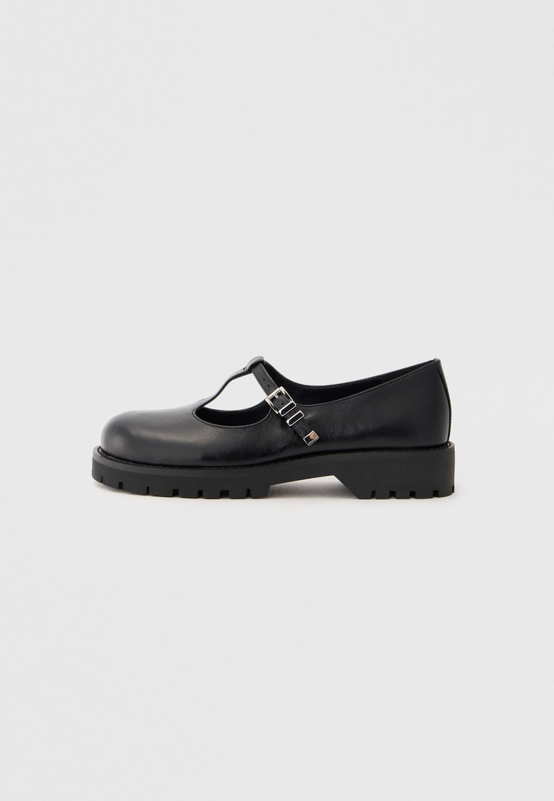 Black leather Mary Jane shoes with a round toe, T-strap design, two adjustable buckles, and a chunky textured sole.