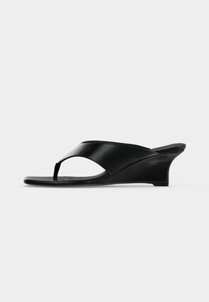 Sandalia cuña de cuero negro con tira tipo tanga y puntera abierta, con un tacón bajo curvado y un diseño minimalista elegante.