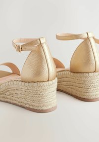 Sandales compensées en cuir doré avec une bride de cheville et une finition texturée, dotées d'une plateforme en jute tressé et d'une semelle intérieure beige lisse.