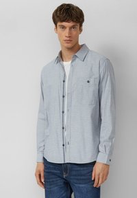 Lichtblauw overhemd met subtiel ruitpatroon, lange mouwen en een borstzak. Voorzien van donkere knopen en contrasterende stiknaden.