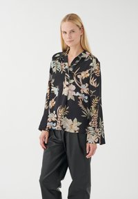 Schwarze Bluse mit langen Ärmeln, versehen mit pastellfarbenen Blumen und Blättern. Der Stoff hat eine glatte Textur und eine lockere Passform.