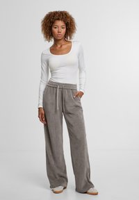 Bílé elastické tričko s dlouhým rukávem spárované s volnými šedými kordovými kalhotami s elastickým pasem a bočními kapsami. Na nohou tenisky.