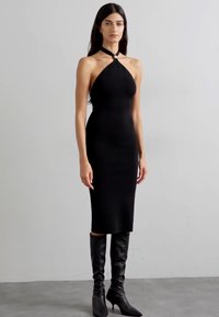 Mustad, keha tooniv midi kleit, millel on halter kaelus ja võtmeaugu detail. Kombineeritud mustade kõrgete kontsadega saapastega. Sile, veniv kangas.