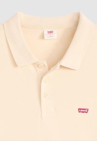 Polo crème en coton texturé, avec un col classique et trois boutons, présentant un logo rouge Levi's sur la poitrine gauche.