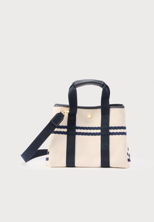 Sac fourre-tout en toile beige avec deux bretelles verticales bleu marine, double poignées, bandoulière longue détachable et rayures horizontales bleu marine près du haut.