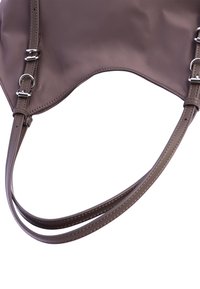 Bolso de mano de nylon marrón con textura suave, que presenta correas ajustables dobles y herrajes en tono plateado. Diseño curvado con líneas limpias.