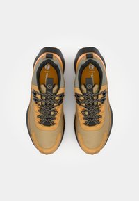 Beżowe i pomarańczowe sneakersy na zewnątrz z sznurowadłami. Cechy to teksturowana tkanina, gumowa podeszwa oraz czarne sznurowadła z odblaskowymi akcentami.