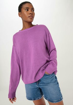 Lila übergroßer Pullover mit Rundhalsausschnitt und eingesetzten Ärmeln, kombiniert mit Jeansshorts. Weiche Textur und lässige Passform.