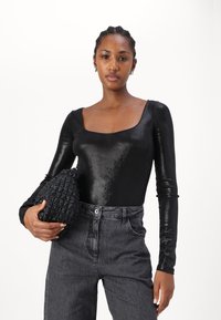 Body nero a manica lunga con scollatura quadrata e tessuto lucido, abbinato a jeans in denim grigi a vita alta e una borsa nera texturizzata.
