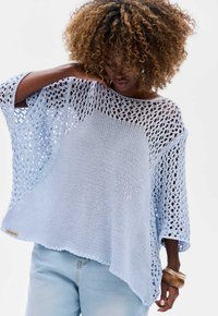 Jasnoniebieski dziergany poncz z otwartym splotem, luźnym krojem i asymetrycznym dołem. Posiada opuszczone rękawy i metkę z boku.