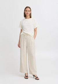 Haut en crème léger à texture, à manches courtes, associé à un pantalon beige à jambes larges, doté d'une taille élastique ajustable et de chaussures à talons noirs avec lanières.