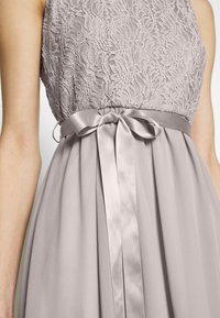 Robe lavande sans manches avec corsage en dentelle florale et jupe lisse, avec un ruban en satin noué en nœud à la taille.