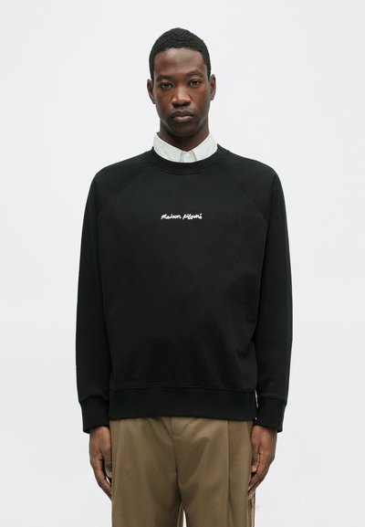 Must hõlmik, millel on raglaankätked ja broderitud "Maison Pléinaire" tekst. Omab ümarat kaelaauku ja pehmeid puuvillaseid materjale.