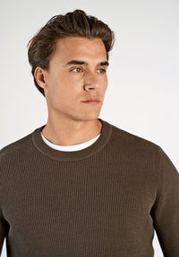 Suéter marrón de canalé con cuello redondo, superpuesto a una camisa blanca, confeccionado en material suave y con un diseño de punto texturizado.