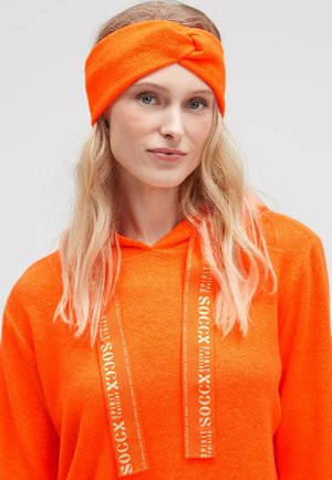 Bright orange fleece headband with a twisted design. Smooth texture and stretchy material. Worn with an orange hoodie featuring logo accents.