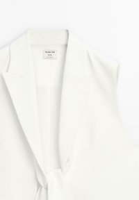 Witte mouwloze blazer met een gesneden kraag en een gestrikt voorontwerp. Gladde textuur met een minimalistische esthetiek en subtiele branding.