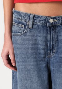 Light blue denim jeans with a high waist, featuring a single front pocket, contrasting stitching, and a metal button closure.