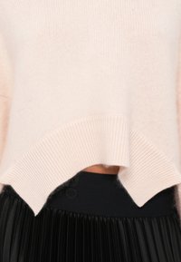 Ανοιχτό ροζ πλεκτό πουλόβερ με ριμπ τελείωμα και διαχωριστική σχεδίαση, συνδυασμένο με μαύρη πλισέ φούστα με υφασμάτινη μέση.