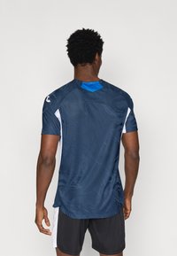 Maglietta atletica blu navy con motivo testurizzato, maniche corte, dettagli bianchi e colletto blu a contrasto, progettata per comfort e prestazioni.