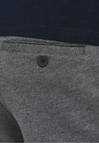 Šedé látkové kalhoty s texturovaným povrchem, se zapínáním na černý knoflík a viditelným lemem námořnicky modré košile nahoře.