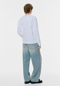 Vit bomullsskjorta med lång ärm och avslappnad passform, kombinerad med ljusblå jeans med vida ben, som har en blekt textur och detaljsömmar.