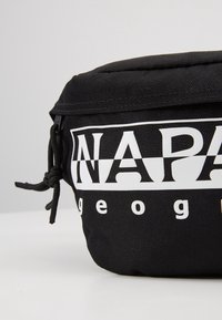 Pochette en tissu noir avec texte partiel blanc "NAP" et "geo" visible, avec une tirette de fermeture éclair nouée sur un fond clair uni.