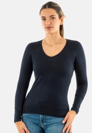 Pull-over ajusté à manches longues bleu marine avec un col en V, texture à côtes et détails de couture subtils. Associé à un jean en denim bleu clair.