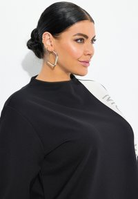 Top in tessuto nero con collo alto, caratterizzato da un pannello bianco a contrasto con testo stampato. Grandi orecchini quadrati in argento completano il look.