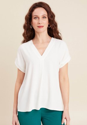 Blouse blanche à manches courtes avec un décolleté en V, présentant des manches remontées et une coupe ample. Texture lisse, ourlet droit et fentes latérales.
