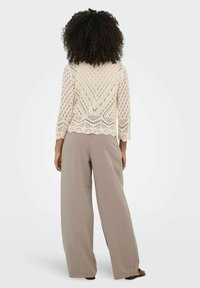 Cremefarbener Häkelstrickoberteil mit 3/4-Ärmeln und gewelltem Saum, kombiniert mit hochtaillierten, hellgrauen, weiten Hosen und minimalistischen Sandalen.