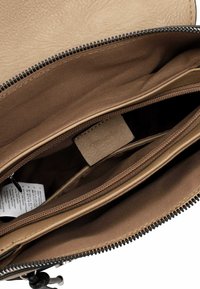 Brown leather bag interior with a zippered compartment, smooth texture, and fabric lining. Includes a tag with brand information and care details.