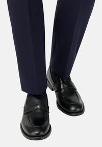 Černé kožené mokasíny s designem zvýšeného pásku, doplněné o tmavě modré krejčovské kalhoty s jemnou texturou a lesklým povrchem.