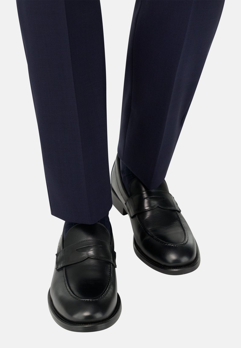 Černé kožené mokasíny s designem zvýšeného pásku, doplněné o tmavě modré krejčovské kalhoty s jemnou texturou a lesklým povrchem.