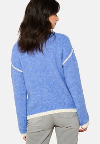 Sininen neulepaita, jossa on pörröinen pinta, vastakkaista kermaista reunusta hihansuissa ja helmassa, sekä rento ja ylisuuri malli.