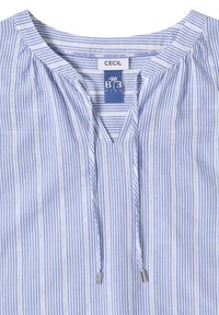 Blouse à rayures verticales bleues et blanches avec col à cordon et étiquettes indiquant « CECIL » et « B.F. KIND » à l'intérieur du col.