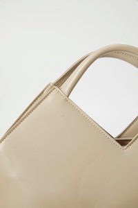 Beige faux leather handbag with structured design, angular shape, and dual handles. Features visible stitching and minimalistic detailing.