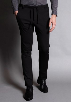 Zwarte op maat gemaakte broeken met een gladde textuur, elastische tailleband en trekkoord, gecombineerd met zwarte nette schoenen.