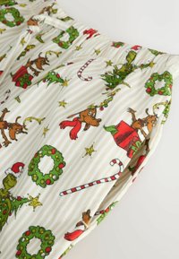 Pantaloni in cotone con stampa natalizia che presenta renne, alberi di Natale, bastoncini di zucchero e ghirlande su uno sfondo a righe beige.