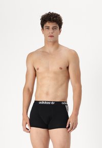 Sorte boksershorts med en tyk elastisk talje, der har hvid "adidas" logo og tre hvide striber på siderne. Fremstillet af bomuldsmateriale, tætsiddende design.