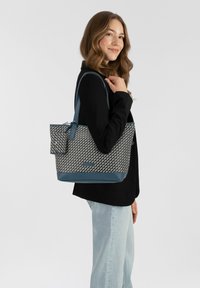 Sac fourre-tout avec un corps en textile à motif beige et marine, un fond lisse marine et des accents. Comprend une petite pochette détachable.