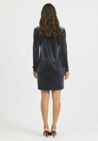 Robe en velours bleu marine foncé avec des manches longues et une silhouette ajustée, longueur genoux à l'arrière, texture lisse et faible éclat.