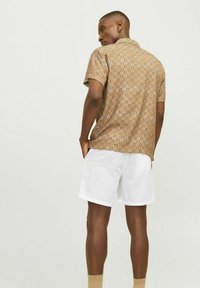 Chemise marron à manches courtes avec un motif géométrique, texture légère et col, associée à un short blanc. Design simple et coupe décontractée.