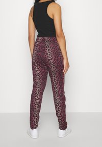 Pantaloni jogger in stampa leopardata nei toni del rosa scuro e viola, con design a gamba affusolata, vita elastica e tasche laterali; abbinati a sneakers bianche.