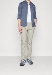 Informele outfit met een marineblauwe button-up shirt, wit T-shirt, beige broek en blauwe New Balance sneakers met witte accenten.