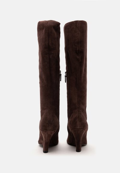 Paire de bottes hautes en suède marron foncé avec des fermetures éclair latérales et des talons hauts et fins, vues de dos sur fond blanc.